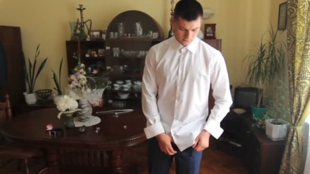 Um tipo bonito veste uma camisa branca. Dia do casamento. homem corre uma camisa em suas calças . — Vídeo de Stock