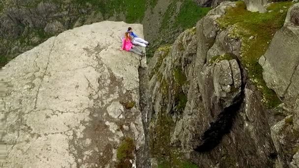 Норвегия. парень и девушка, сидящие на краю Тролля — стоковое видео