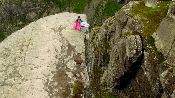 Norge. kille och tjej sitter på kanten av Trolltunga — Stockvideo