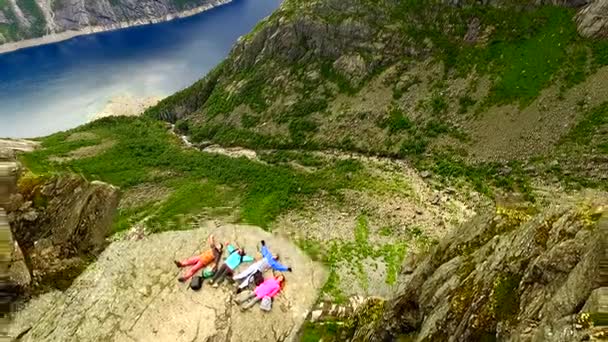 Noruega. Dois tipos e duas raparigas estão deitados à beira do penhasco. Trolltunga — Vídeo de Stock