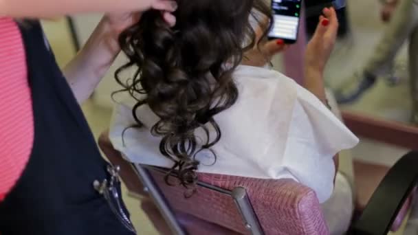 La fille fait une coiffure chez le coiffeur et regarde à travers son iPhone . — Video