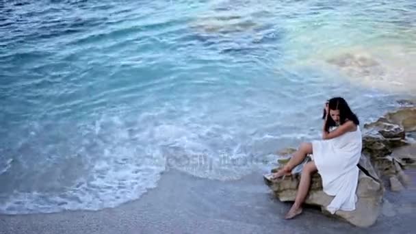 Hermosa chica en vestido blanco está sentado en la playa. Países Bajos — Vídeos de Stock