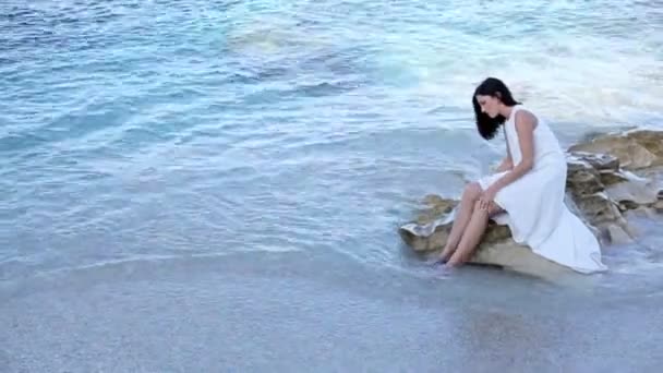 Schönes Mädchen in weißem Kleid sitzt am Strand. Griechenland — Stockvideo