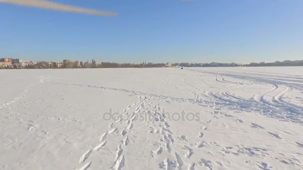 Drone vliegt over een bevroren meer in de buurt van een stadspark op de achtergrond van een stad van de winter in duidelijke zonnig weer — Stockvideo