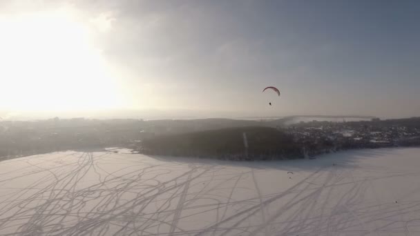 มุมมองทางอากาศ การแข่งขันนักบิน paragliding บนทะเลสาบน้ําแข็งใกล้สวนสาธารณะเมือง . — วีดีโอสต็อก