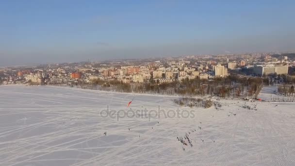 Εναέρια άποψη. Διαγωνισμοί πιλότους αλεξίπτωτο πλαγιάς σε μια παγωμένη λίμνη κοντά στο πάρκο της πόλης. — Αρχείο Βίντεο