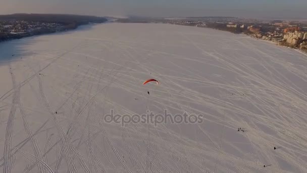 鸟瞰图。伞的竞争飞行员在一个结冰的湖在城市公园附近在天的日落 — 图库视频影像