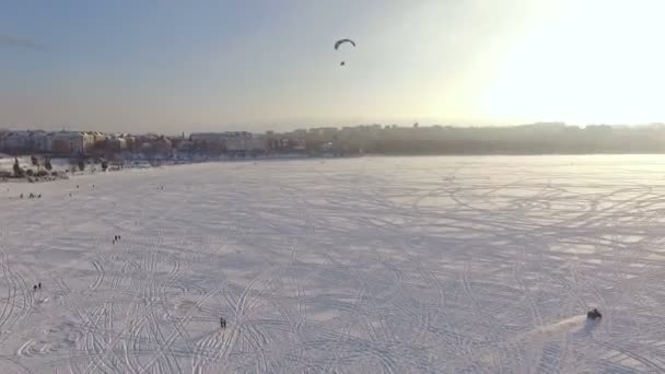 Вид сверху. Соревнования летчиков параплана на замерзшем озере возле городского парка на закате дня — стоковое видео