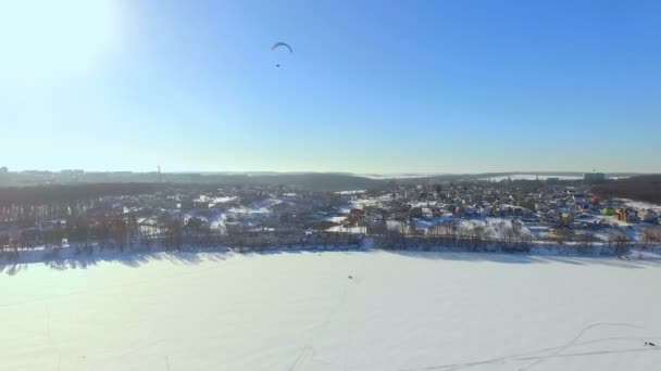 Paesaggio invernale. Bella vista sulla città invernale e sul lago da una vista a volo d'uccello. parapendio vola sopra un lago ghiacciato — Video Stock