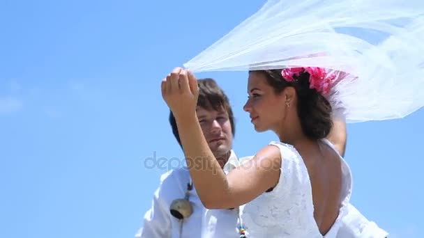 Hermosos novios en la playa. Velo novias maravillosamente revoloteando en el viento — Vídeo de stock