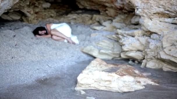 Испуганная девушка лежит на песке в каменном гроте — стоковое видео
