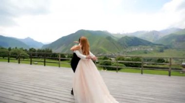 Gelin kollarında tutarak ve dağlar, Kazbegi, Gürcistan otelin ahşap Teras daire çizerek damat 