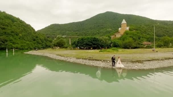 リバーサイド ジョージアに立っている花嫁の近くに水に小石をスキップして新郎の航空写真 — ストック動画