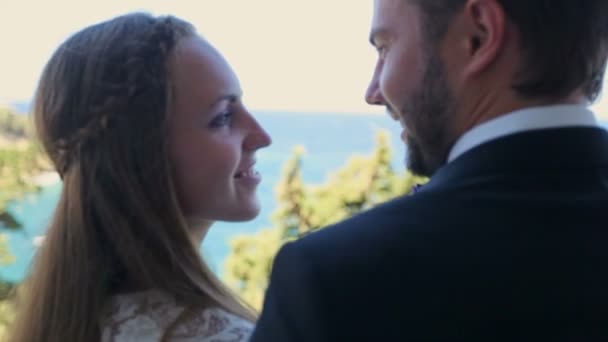 結婚式の日の概念 背景にギリシャの海岸のホテルのバルコニーに寄り添う新郎新婦 — ストック動画
