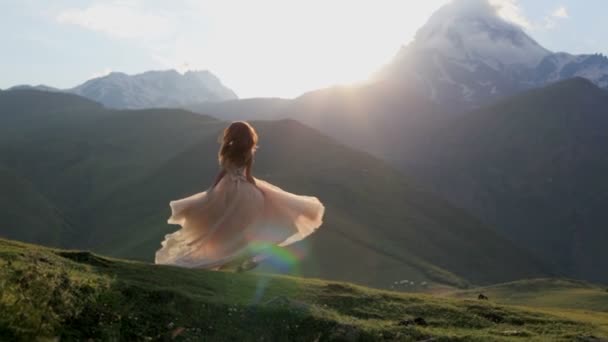 Красивая девушка в шикарном платье танцует вечером на фоне гор и заходящего солнца — стоковое видео