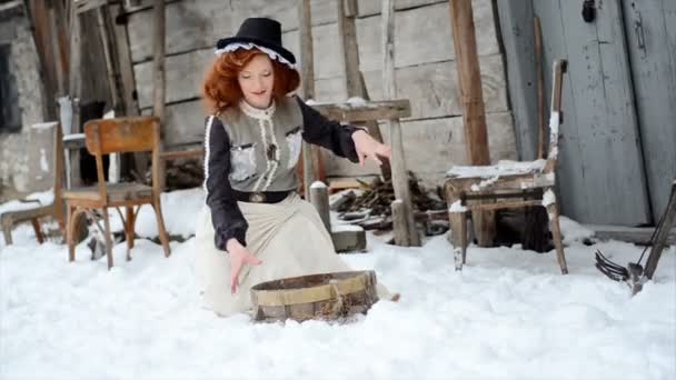 Chica en un vestido de cuento de hadas está de pie junto a la vieja casa de madera y arrojando nieve — Vídeos de Stock