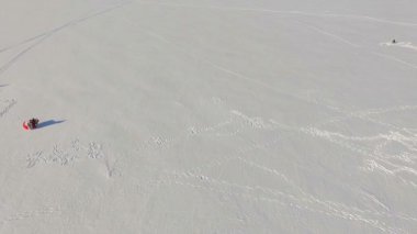 Kışın donmuş gölün havadan görünüşü, paraşütlü paraşütçüler, bir kar aracı ve delikte bir balıkçı..