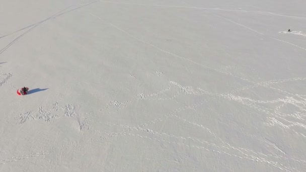 Luftaufnahme eines zugefrorenen Sees im Winter, Gleitschirme mit Fallschirm, Schneemobil und Fischer am Loch. — Stockvideo