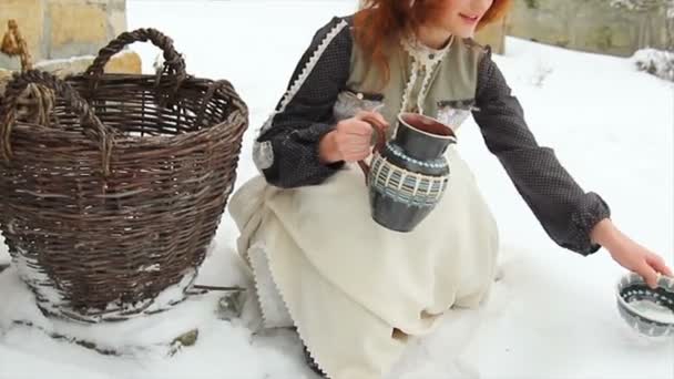 Красивая рыжая девушка в этнической одежде наливает молоко собаке в тарелку. — стоковое видео