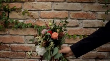 Gelin ve damat kırmızı tuğladan bir duvarın arkasında bir buket tutuyorlar.