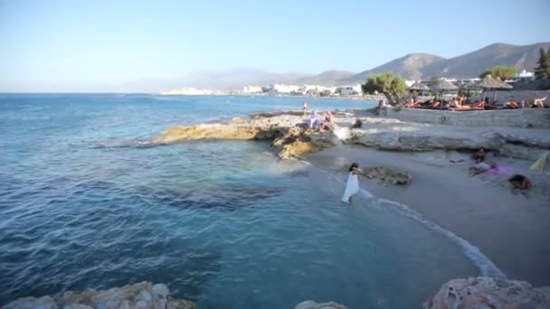 Красивая брюнетка в белом платье стоит на берегу моря и наслаждается морским ветром и морем — стоковое видео