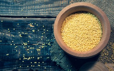 Raw dry millet is scattered over a wooden bowl. Millet uncooked grains in a wooden bowl on a wooden table. Healthy food vegan food concept.