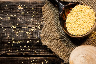 Raw dry millet is scattered over a wooden bowl. Millet uncooked grains in a wooden bowl on a wooden table. Healthy food vegan food concept.