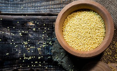 Raw dry millet is scattered over a wooden bowl. Millet uncooked grains in a wooden bowl on a wooden table. Healthy food vegan food concept.