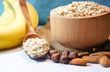 Tahta bir kasede yulaf ezmesi ve kaşıkla muz, fındık ve tarçınlı sağlıklı vejetaryen kahvaltısı.