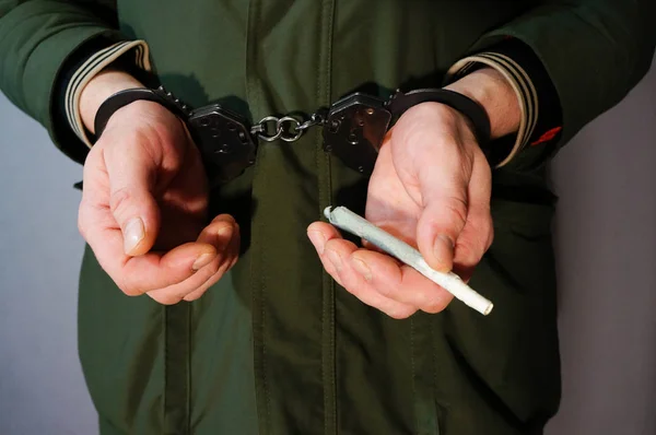 Uyuşturucudan tutuklanmış, elleri kelepçeli, elinde marihuana olan bir sigara, yasaları çiğnemiş.