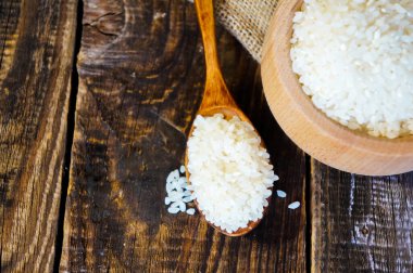 Tahta bir arka planda tahta bir kaşıkta bir torba kumaş ile Türk çiğ pirinç taneleri.