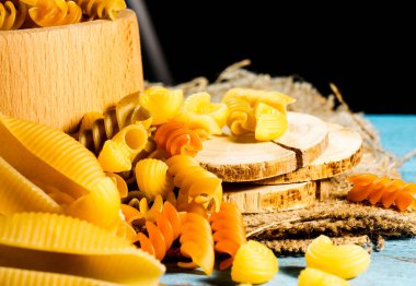 Ahşap arka planda mavi renkli çeşitli makarna çeşitleri. Farfalle, fettuccine, noodle, fusilli ve penne.