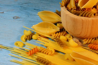 Ahşap arka planda mavi renkli çeşitli makarna çeşitleri. Farfalle, fettuccine, noodle, fusilli ve penne.
