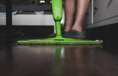 Adam koyu ahşap zemini yeşil bir paspasla yıkıyor. Ev temizliği kavramı