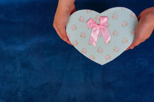 gift box in the form of a heart in the hands of a girl on a blue background, concept of love