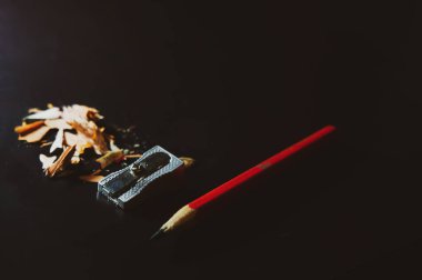 Kırmızı ahşap kalem, bileyici ve siyah arka planda talaş.