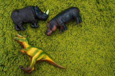  Oyuncak dinozor su aygırı ve gergedan yeşil halıda metnin için yer var..