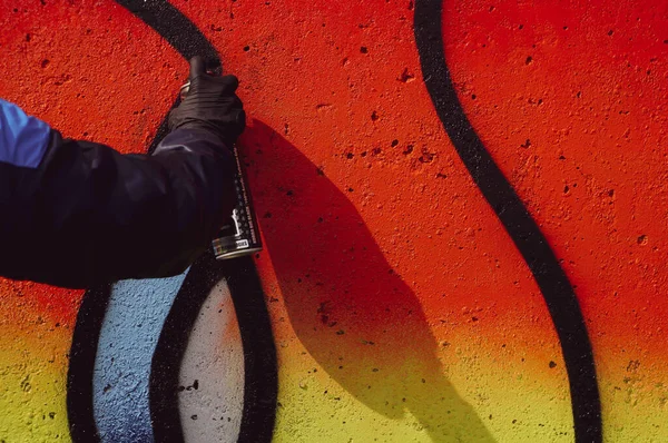 Street artist paints colorful graffiti on a common wall - Modern art concept, hand with a sprayer spray paint on the wall