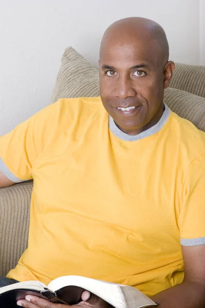 African American człowiek siedzi na kanapie i czytanie. — Zdjęcie stockowe