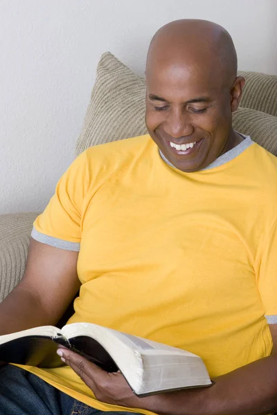 Afro-amerikai ember ül a kanapén, és az olvasás. — Stock Fotó