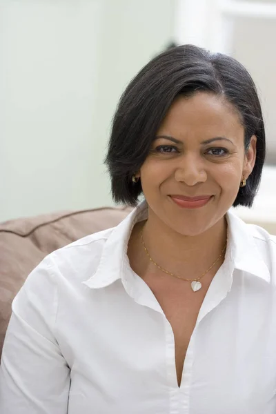 Mujer madura sonriente sentada en su sofá . — Foto de Stock