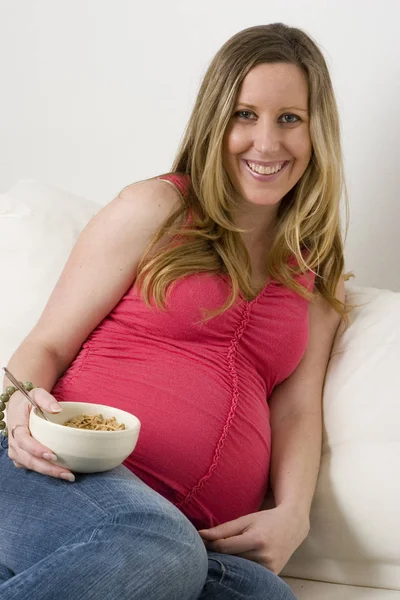 Werdende Mutter sitzt auf dem Sofa und isst Müsli. — Stockfoto