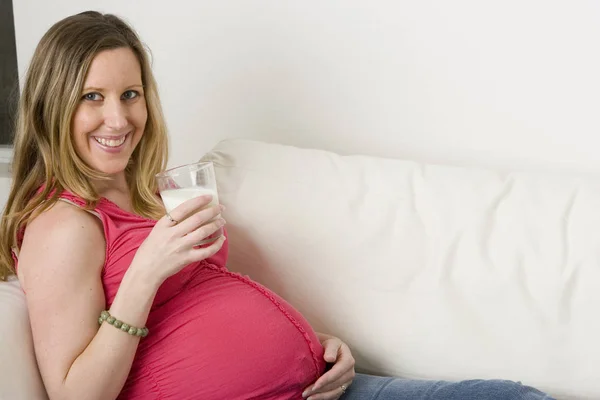 Werdende Mutter sitzt auf dem Sofa und trinkt Milch. — Stockfoto