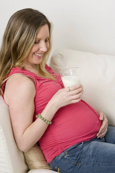 Várandós anya ül a kanapén, fogyasztói tej. — Stock Fotó