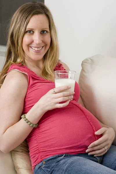 Werdende Mutter sitzt auf dem Sofa und trinkt Milch. — Stockfoto