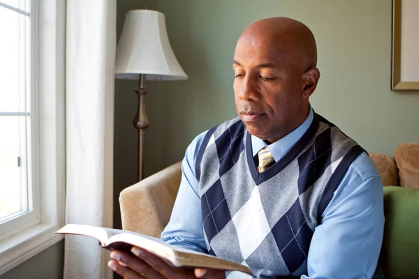 Uomo afroamericano seduto su un divano a leggere . — Foto Stock