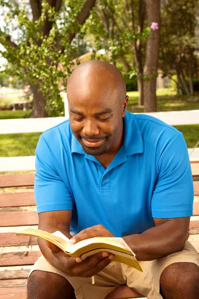 Hombre afroamericano sentado en un banco y leyendo . —  Fotos de Stock