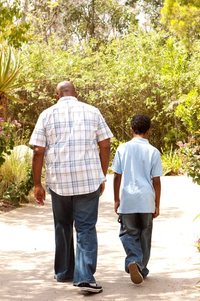 Achteraanzicht van een Afrikaanse Amerikaanse vader en zoon een wandeling. — Stockfoto