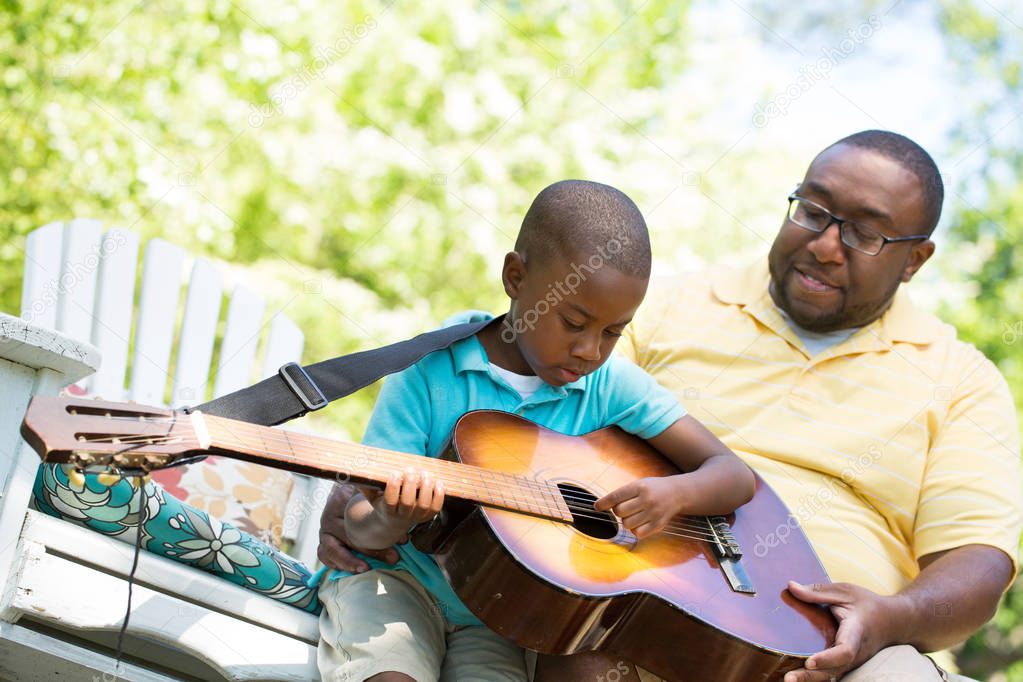 Father teaaching his his son to play the guitar.