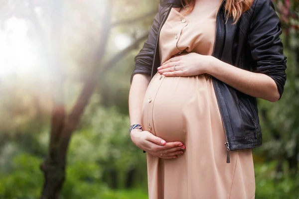 Terhes nő bézs ruhát és fekete kabátot visel, tavasszal virágzó fa mellett áll. Közelről. kivágott kép — Stock Fotó